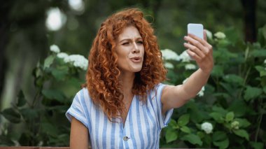 Kıvırcık saçlı kadın yeşil parkta selfie çekiyor. 