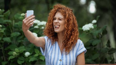 Yeşil parkta selfie çekerken dilini çıkaran komik kızıl kadın. 