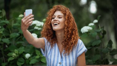 Mutlu kızıl saçlı kadın yeşil parkta selfie çekiyor. 