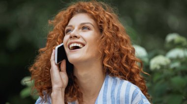 Mutlu, kızıl saçlı genç bir kadın. Akıllı telefondan konuşurken gülüyor. 