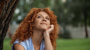 dreamy woman with curly hair looking up and smiling in park clipart