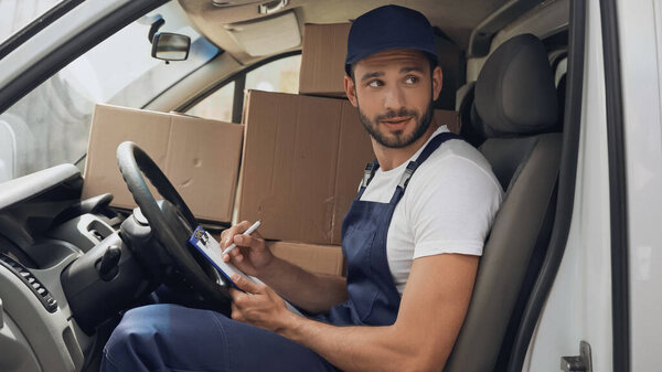 Courier writing on clipboard near carton boxes in car 