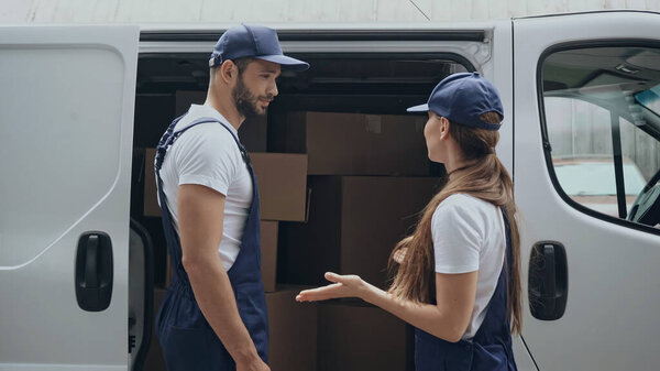 Delivery woman talking to colleague near carton boxes in car outdoors 