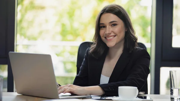 在办公室用笔记本电脑打字的年轻而快乐的女商人 — 图库照片