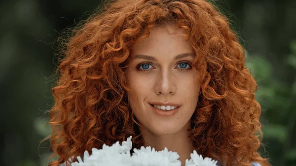 白い花の近くに青い目をした笑顔の赤毛の女性 — ストック写真