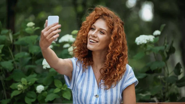 Yeşil parkta selfie çeken mutlu kızıl kadın. 