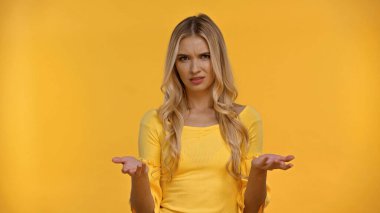 Confused blonde woman in blouse pointing with hands isolated on yellow  clipart