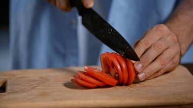 Kesme tahtasında olgun domatesleri kesen adamın yakın görüntüsü