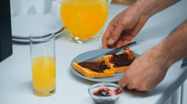 Taze portakal suyunun yanındaki adamın kısmi görüntüsü ve mutfakta reçelli tost.