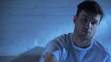 Tişörtlü bir adam uykusuz bir gecede yatak odasında oturuyor.