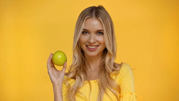 Positiv Blond Kvinna Tittar Kameran Och Håller Äpple Isolerat Gul — Stockfoto