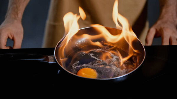 обрезанный вид человека, жарящего куриное яйцо с огнем на сковороде 