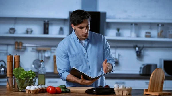 Young Man Reading Cookbook While Standing Table Fresh Ingredients — Stock Photo, Image