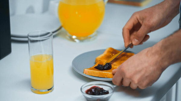 частичный вид человека, готовящего тосты с конфитюром рядом с апельсиновым соком