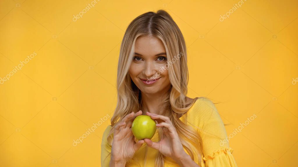 Smiling blonde woman holding fresh apple isolated on yellow