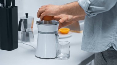 cropped view of man squeezing fresh orange on electric juicer near glass  clipart
