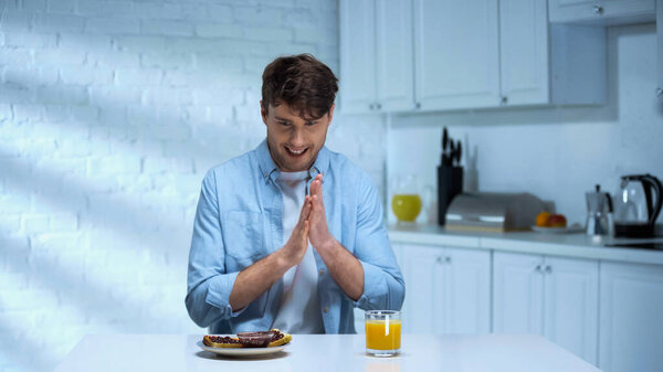 pleased man rubbing hands near toasts with confiture and orange juice in kitchen