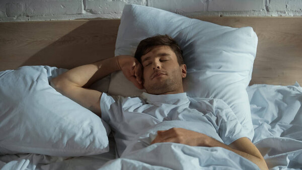 sleeping man lying on white bedding in morning