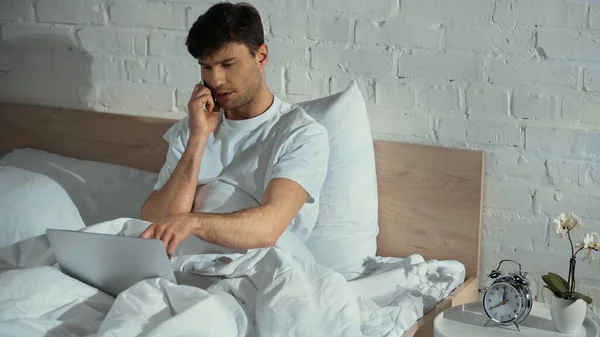 Pria Menunjuk Laptop Saat Berbicara Smartphone Tempat Tidur — Stok Foto