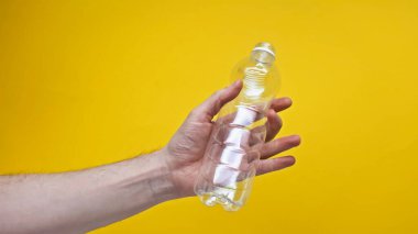 Kırpılmış görüntüde plastik şişe tutan adam sarıda izole edilmiş. 