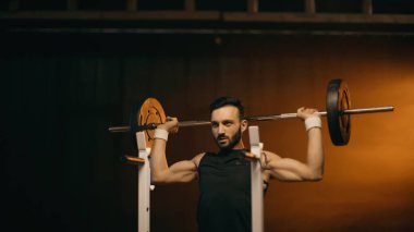 Kas sporcusu koyu arkaplanda halterle çalışıyor.
