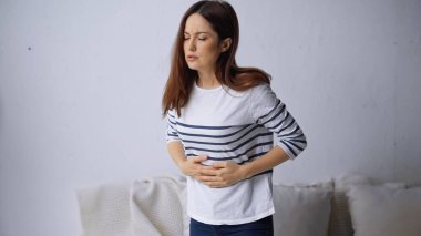 brunette woman standing with closed eyes and suffering from abdominal pain clipart