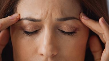 Kapalı gözlü kadının migren ağrısı çekerken kafaya dokunuşunu yakından izle.