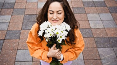 high angle view of happy woman with closed eyed smelling white flowers outside 
