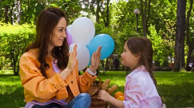 happy mother and daughter playing patty cake game in park clipart