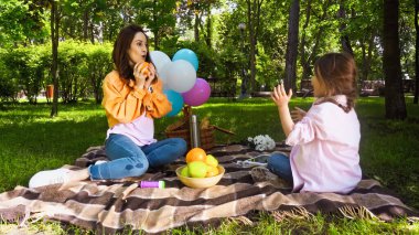surprised mother holding orange and looking at daughter during picnic 