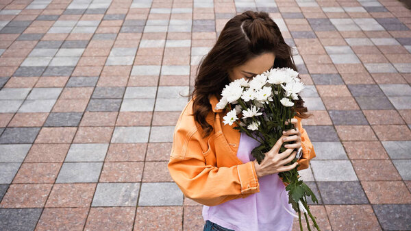 high angle view of brunette woman smelling white flowers outside 