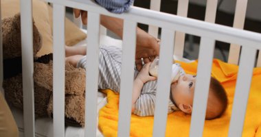 father holding baby bottle and feeding infant son in crib