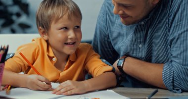 Mutlu baba, evdeki kağıda resim çizen oğluna bakıyor.