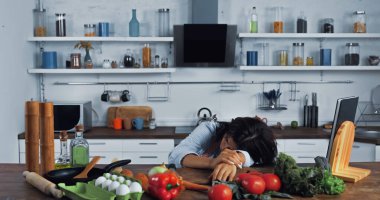 tired woman lying near fresh vegetables and eggs on kitchen worktop