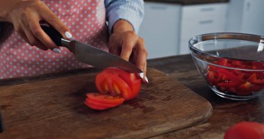 cropped view of woman cutting red tomato near bowl with chopped bell pepper