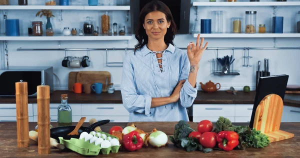 happy tattooed woman showing okay sign near raw ingredients and cooking utensils