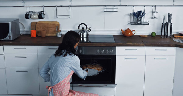брюнетка женщина печет сладкий пирог в электрической духовке дома