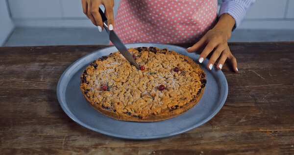 cropped view of woman cutting baked pie on tray in kitchen