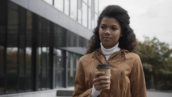 young african american woman walking with coffee to go on street