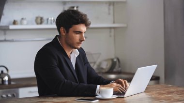 freelancer using laptop near smartphone and cup of coffee on desk