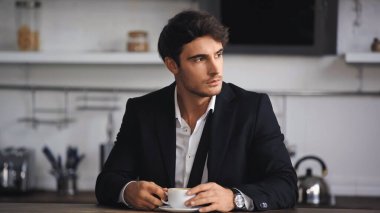 Resmi olarak işadamı mutfakta otururken elinde bir fincan kahve taşır. 