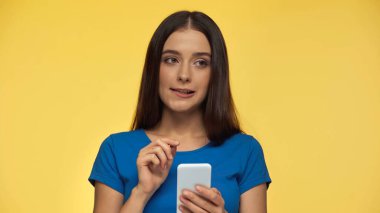 Kafası karışmış, mavi tişörtlü, elinde akıllı telefon tutan esmer bir kadın.