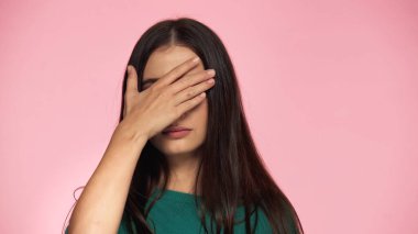 brunette young woman in green blouse covering eyes with hand isolated on pink 