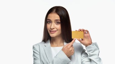 Gri ceketli başarılı bir iş kadını. Gülümsüyor ve beyaza izole edilmiş kredi kartını işaret ediyor.
