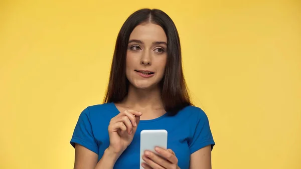 Puzzled Young Brunette Woman Blue Shirt Holding Smartphone Isolated Yellow — Foto de Stock