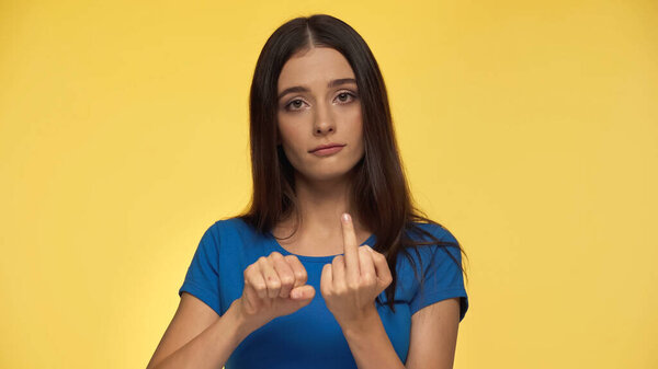 rude young woman in blue t-shirt showing middle finger isolated on yellow