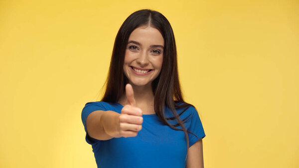 young and happy woman in blue t-shirt showing thumb up isolated on yellow