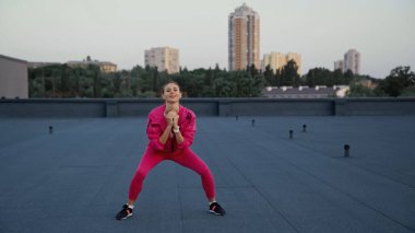 Smiling sportswoman training and looking at camera on roof 