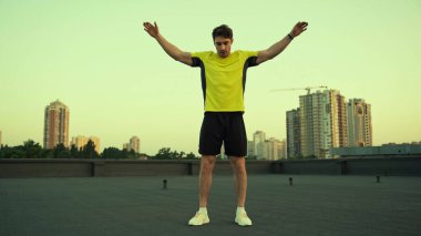 Young sportsman working out on roof of building in evening 