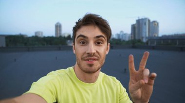Sportsman looking at camera while showing peace sign on roof in evening 